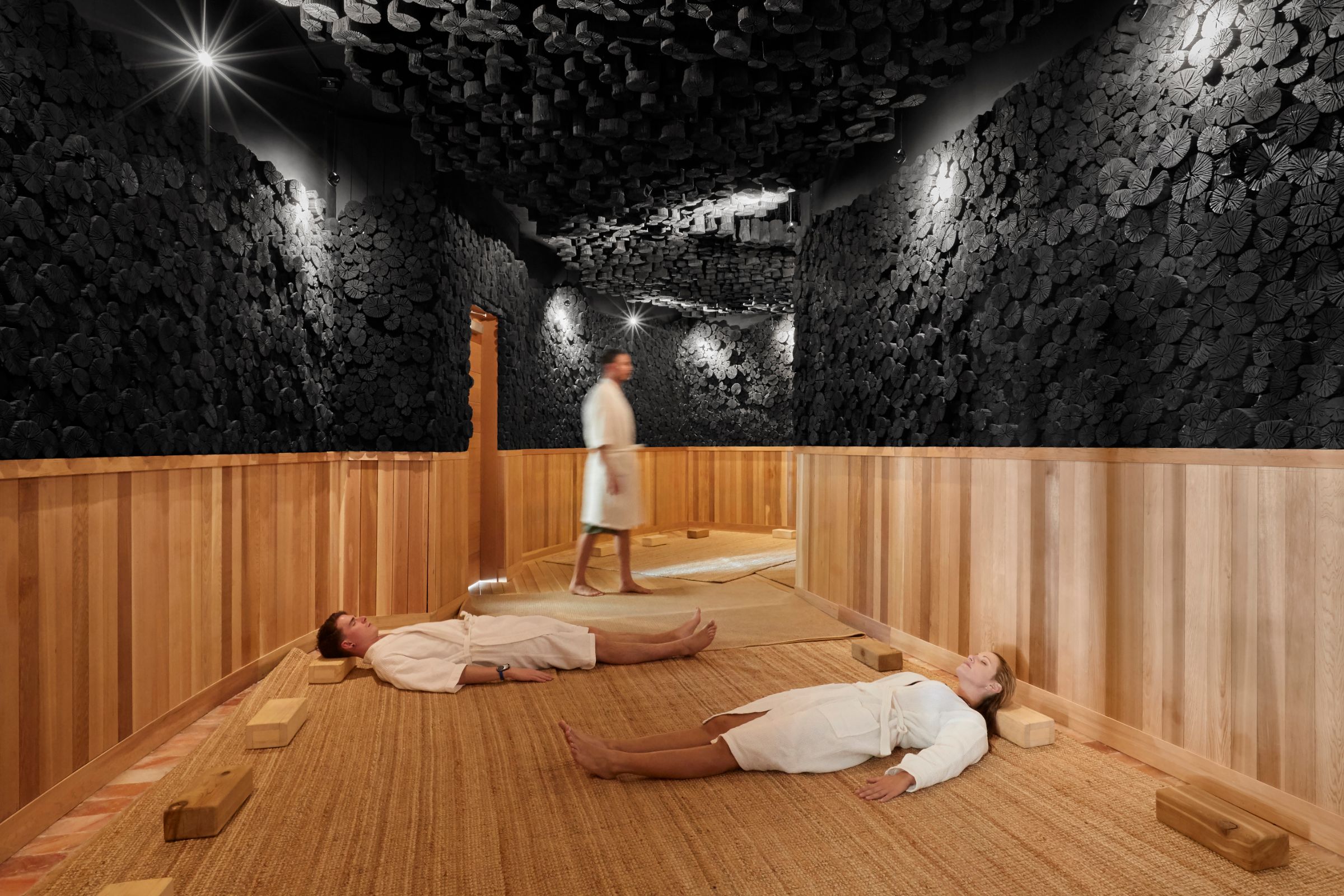 Two people relaxing in the charcoal sauna at Sojo Spa Club as another person enters the sauna room