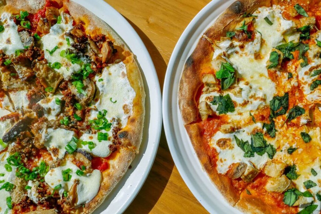 A mushroom sausage pizza and chicken vodka pizza on a wood table