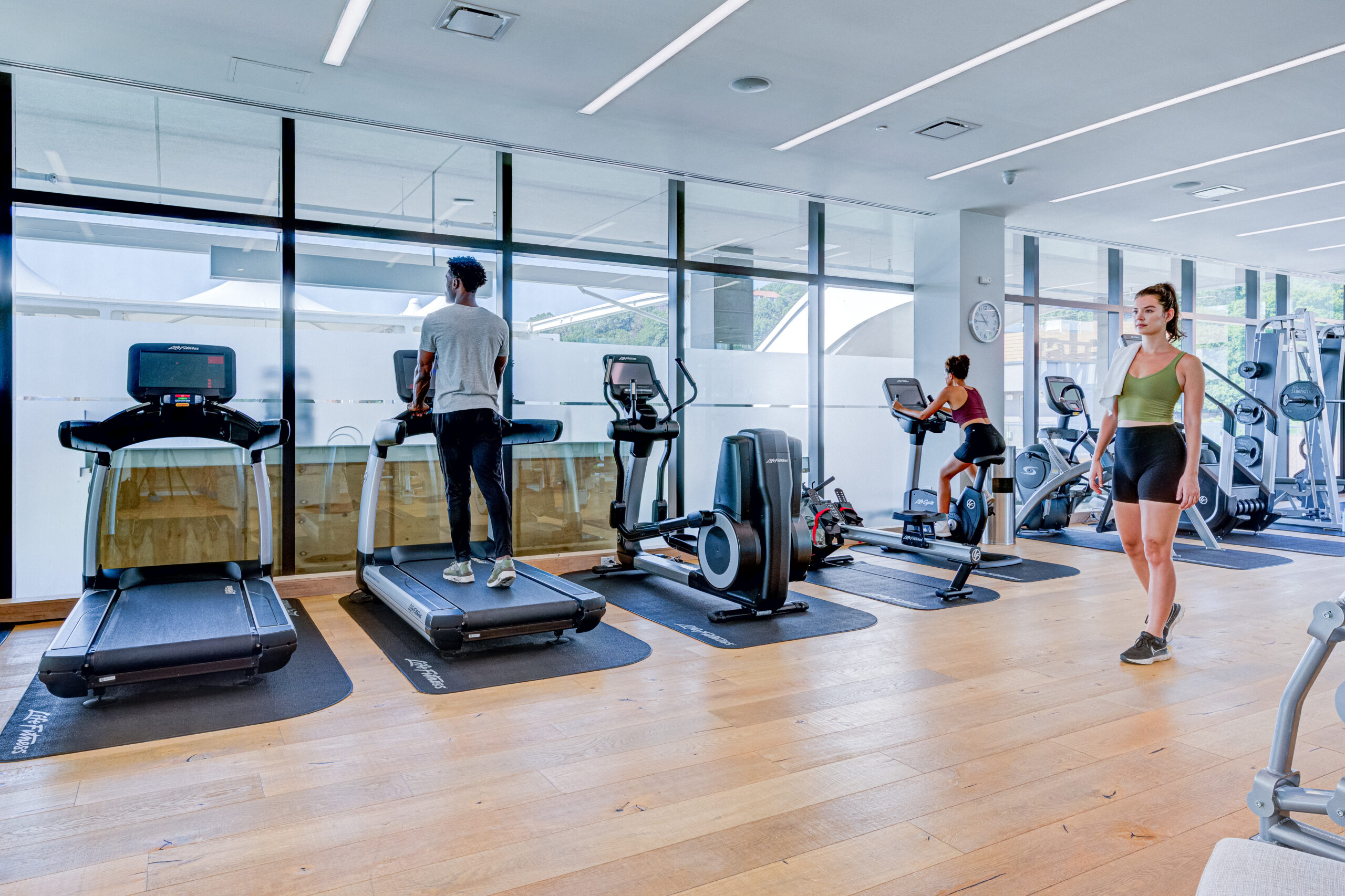 A woman and man work out, while another woman passes by, in the Fitness Center at SoJo Spa Club